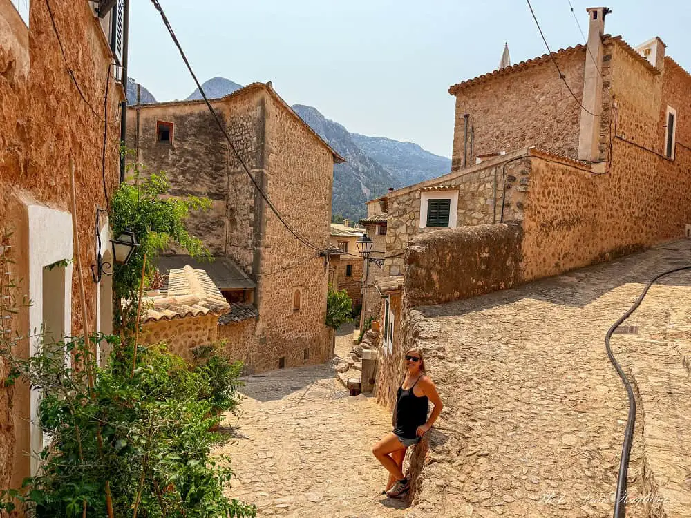 Me standing in a cobbled street with old stone houses in Fornalutx, which is one of the most underrated stops on a Mallorca road trip.