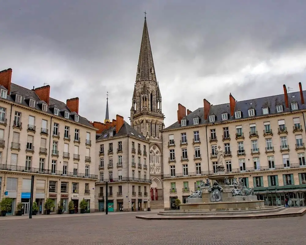 Royal square with fountain and church tower in Nantes city in France