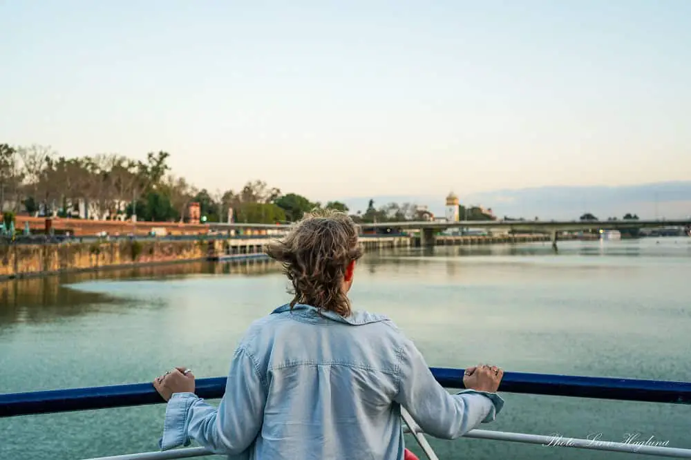Me standing on the front of a boat, looking at the water on a Seville boat cruise on the Guadalquivir River during sunset. If you're looking for what to do in Seville in the evening, this is the perfect thing to do at sunset.