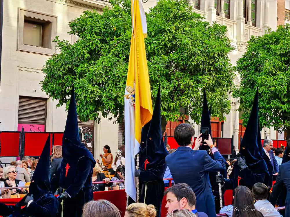 Nazarenos dressed in black with pointy hats in Seville during a Semana Santa parade. This is one of the most unique things to experience in Seville, as one of the biggest easter celebrations in the country.