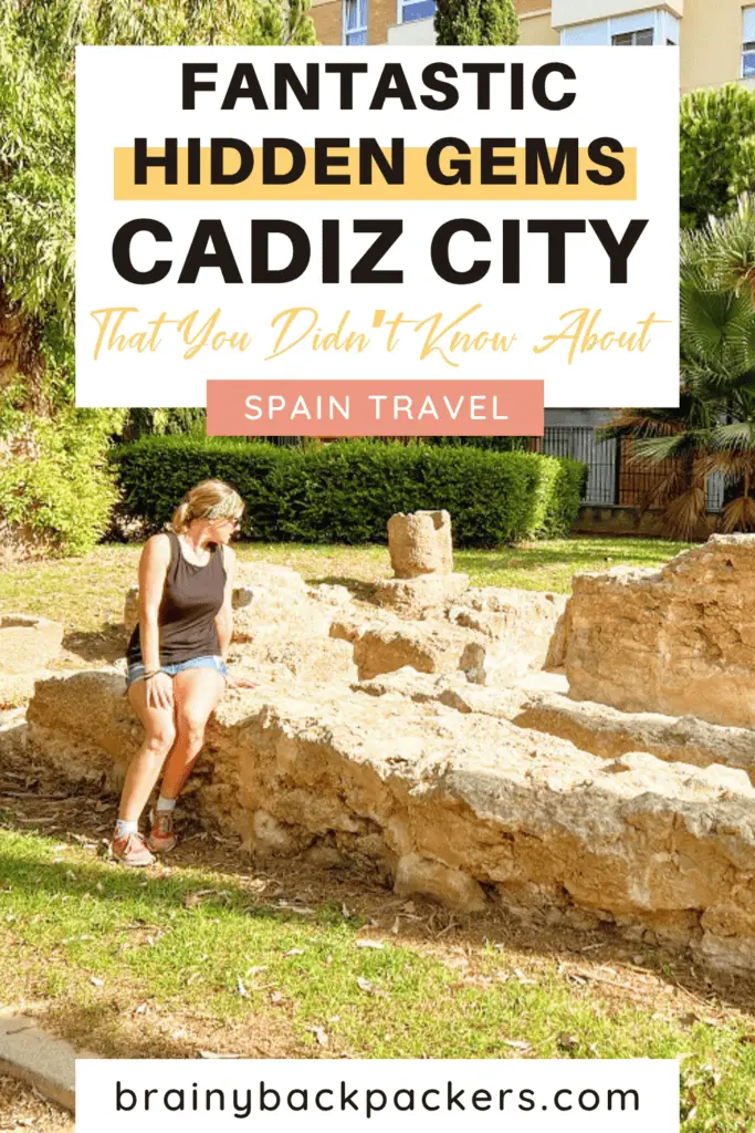 Me, in sunnies, jeans shorts, and a black sleeveless top, sitting on the ancient ruins of a tomb in a park, which is one of the hidden gems in Cádiz, Spain that you didn't know about.