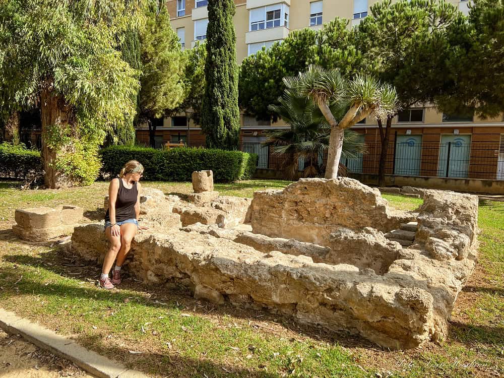 Me sitting on Phunic remains of a tomb which is a true Cadiz hidden gem. It's a sunny day and green grass and trees surround the ruins.