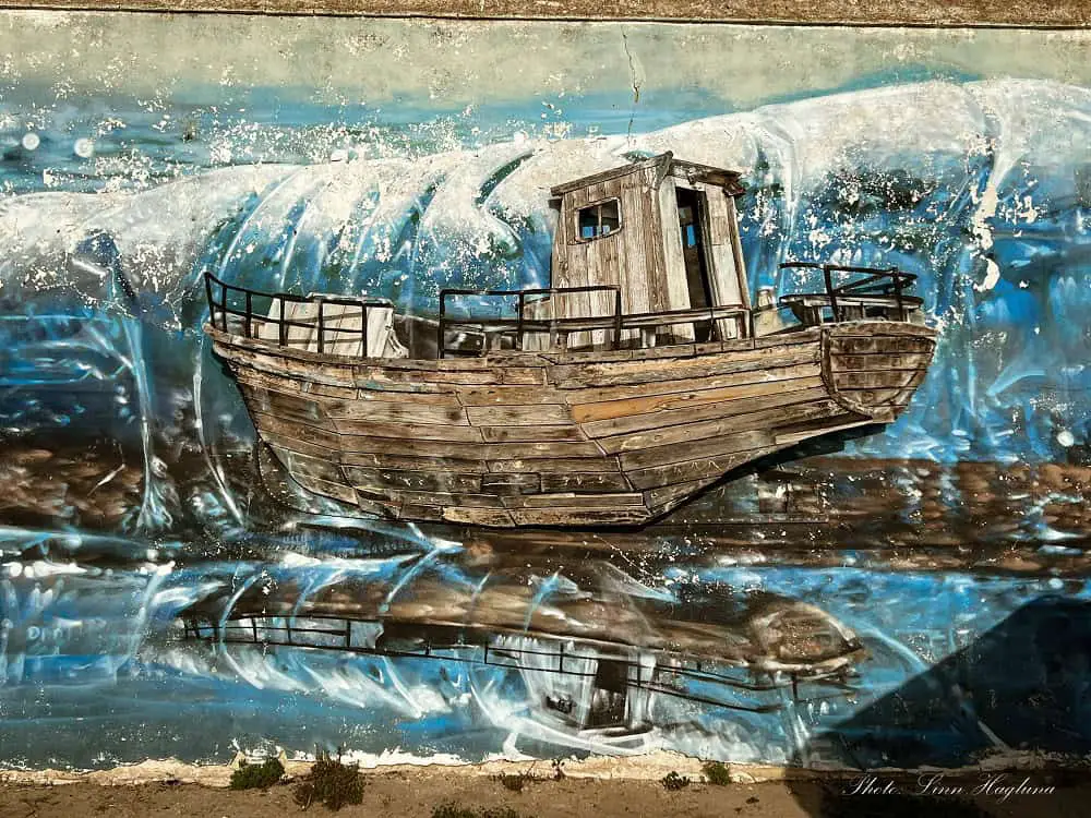 Street art featuring a wooden boat sticking out of a painting of the blue sea with heavy waves in Cadiz city in Andalucia, Spain.