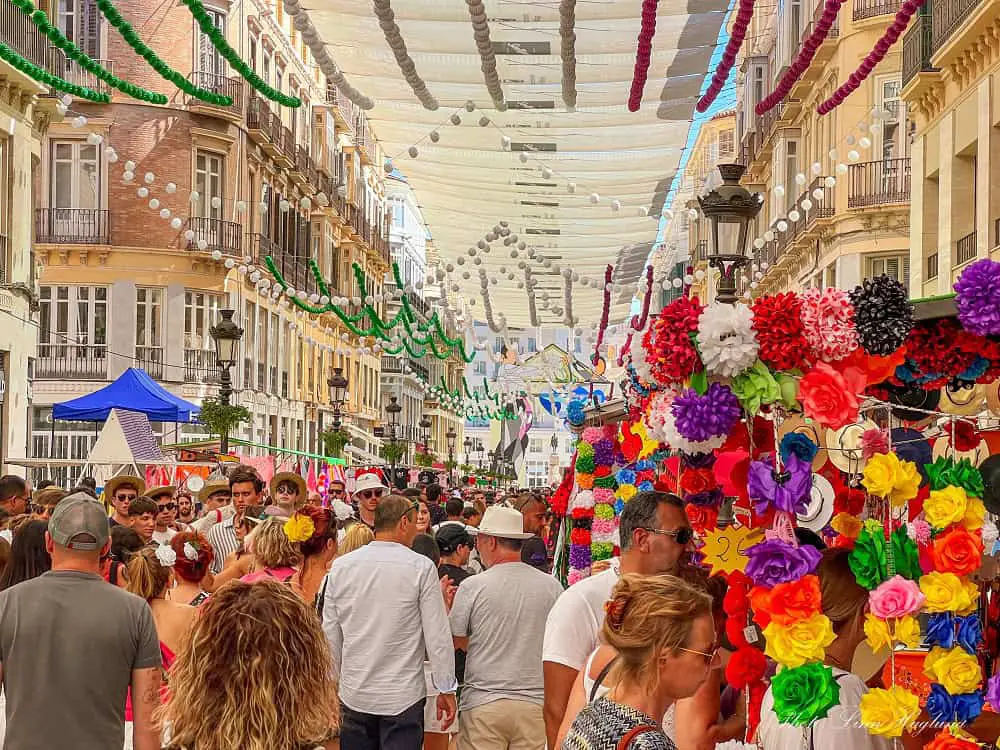 People walking in the street during Malaga Fair with colorful decorations in the street.