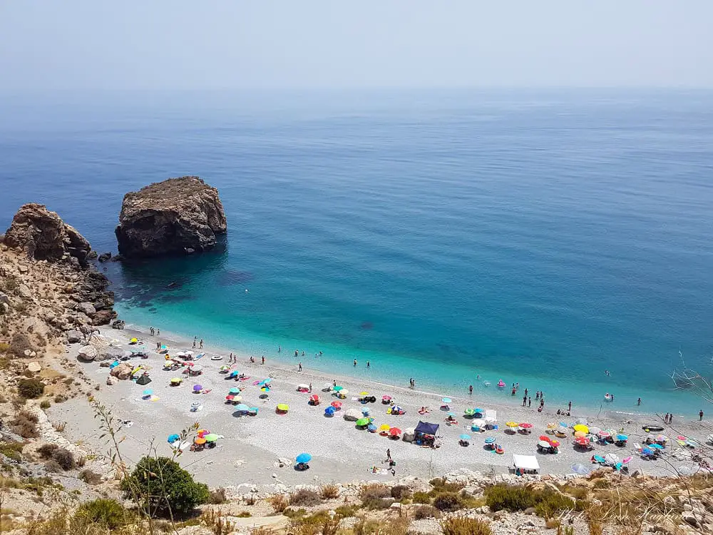 Rijana Beach dotted with people and colorful parasols, easily one of the most beautiful Granada beaches with turquoise water.