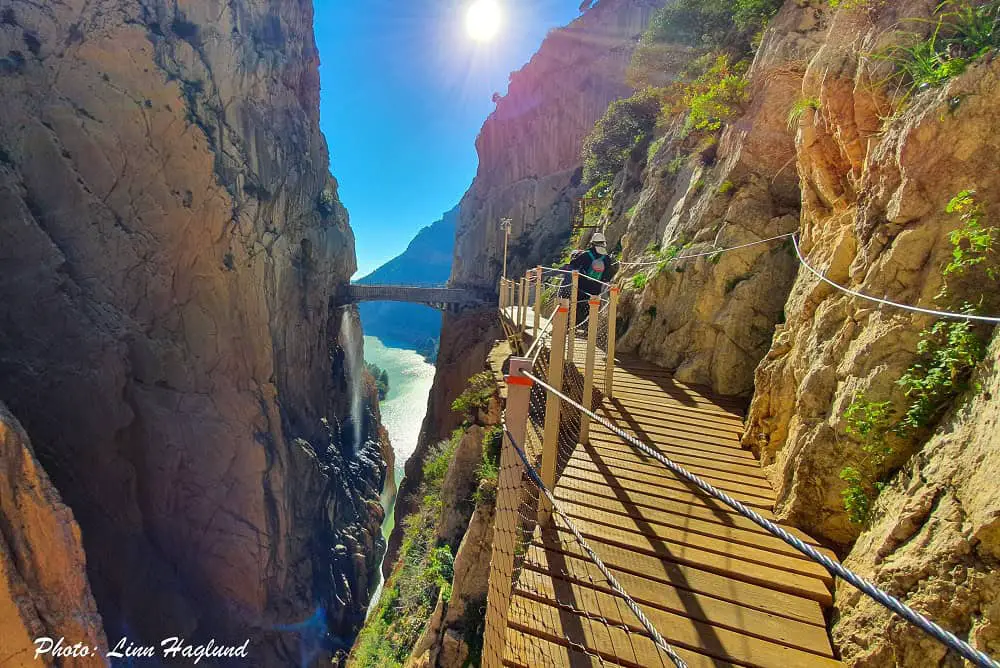 A wooden path along the mountain inside a deep gorge leading to a hanging bridge crossing the gorge - a true Spain bucket list experience!