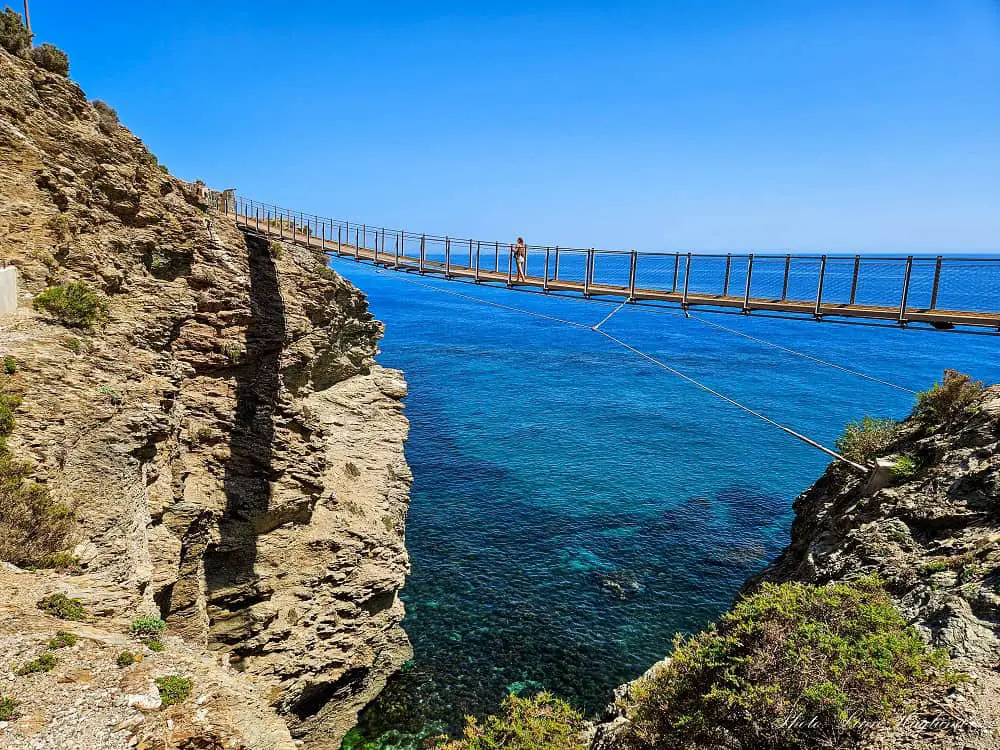 Me crossing a long suspension bridge above the glittering Mediterranean Sea.