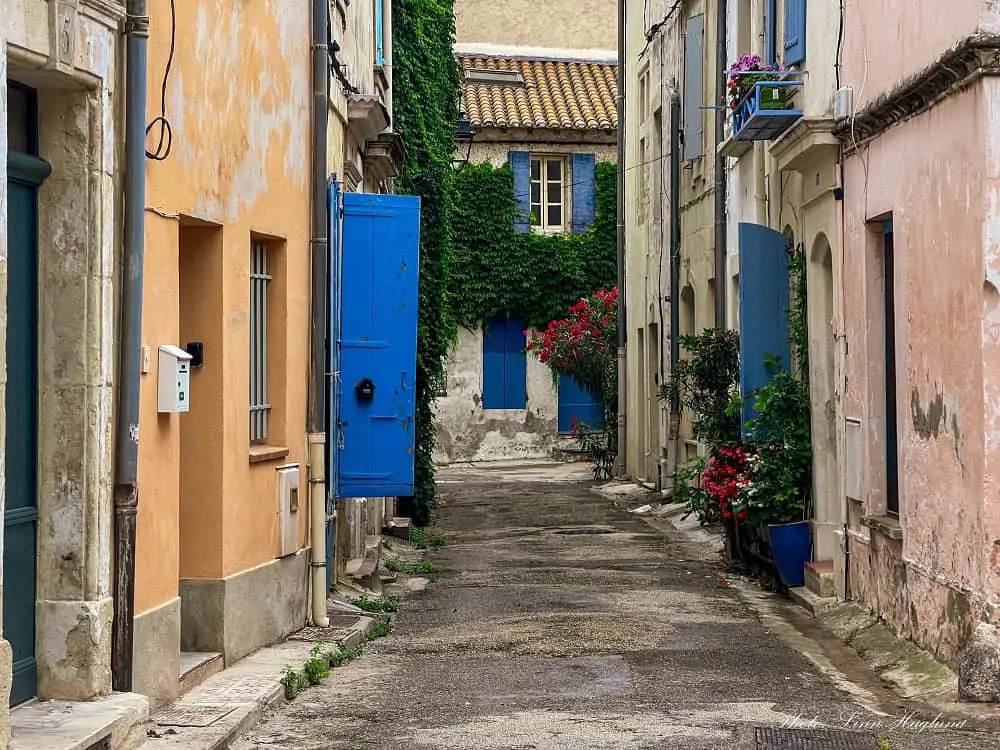 Beautiful street in Arles France with wooden, bluepainted window covers and green plants draped down the pastel-colored walls.