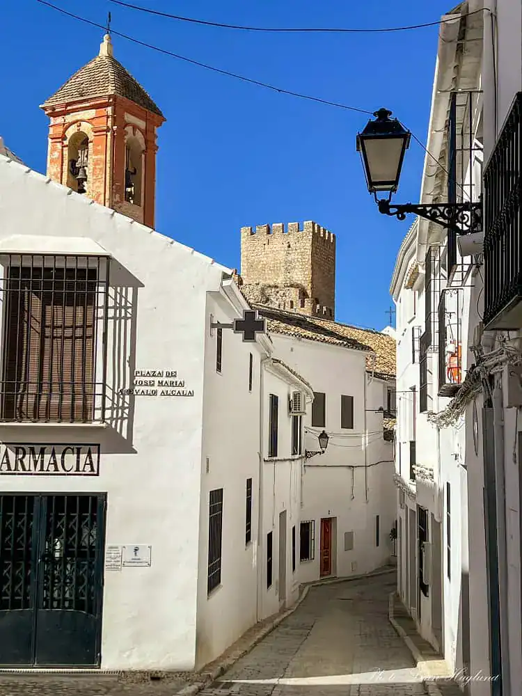 Streets of Zuheros Cordoba with whitewqashed houses and a red church tower and a watch tower seen above the houses.
