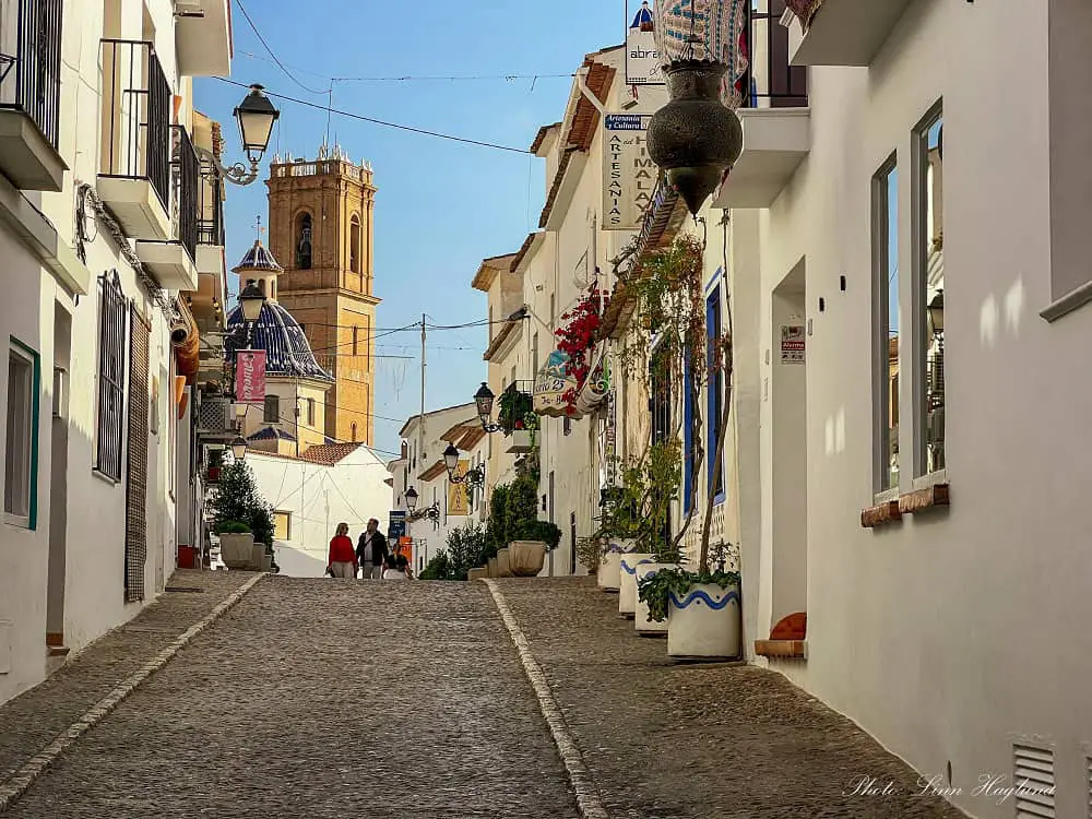 Cobbled street leading to a church square witrh a blue dome in Altea village.