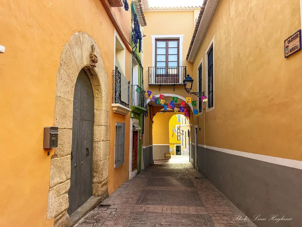 An arch with a window crossing a narrow street with pastel colored housewalls on both sides in Carrer Arxiu in Villajoyosa.