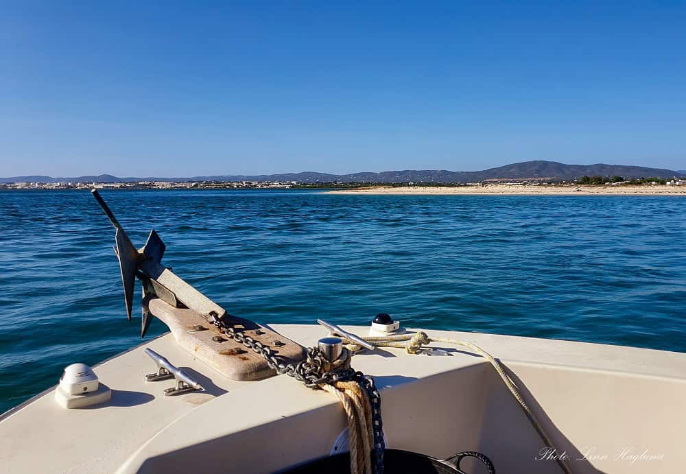 The front of a white boat heading towards a sandy island outside Faro in southern Portugal on a sunny day. Taking one of these Faro boat tours to the barrier islands is one of the best things to do in Faro.
