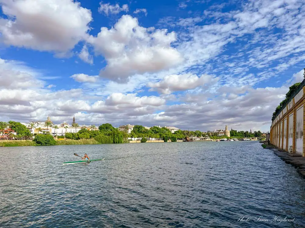 People on a Seville river cruise and others kayaking in the Guadalquivir River in Seville.