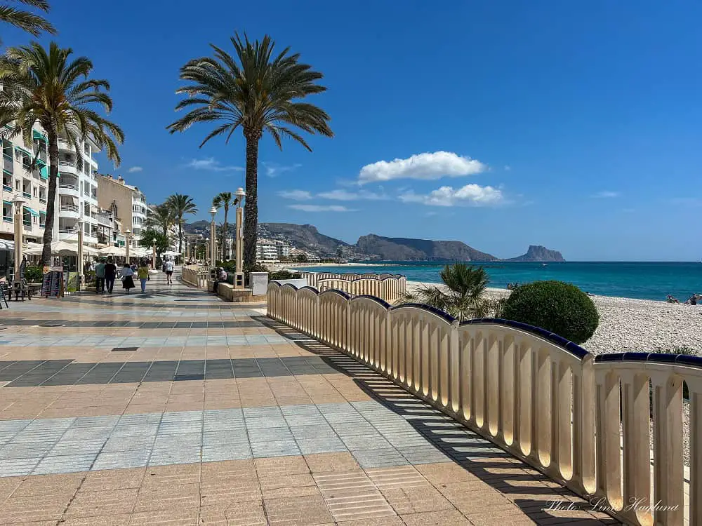 Altea beach promenade along a pebbled beach and views of mountains jutting into the sea further ahead.
