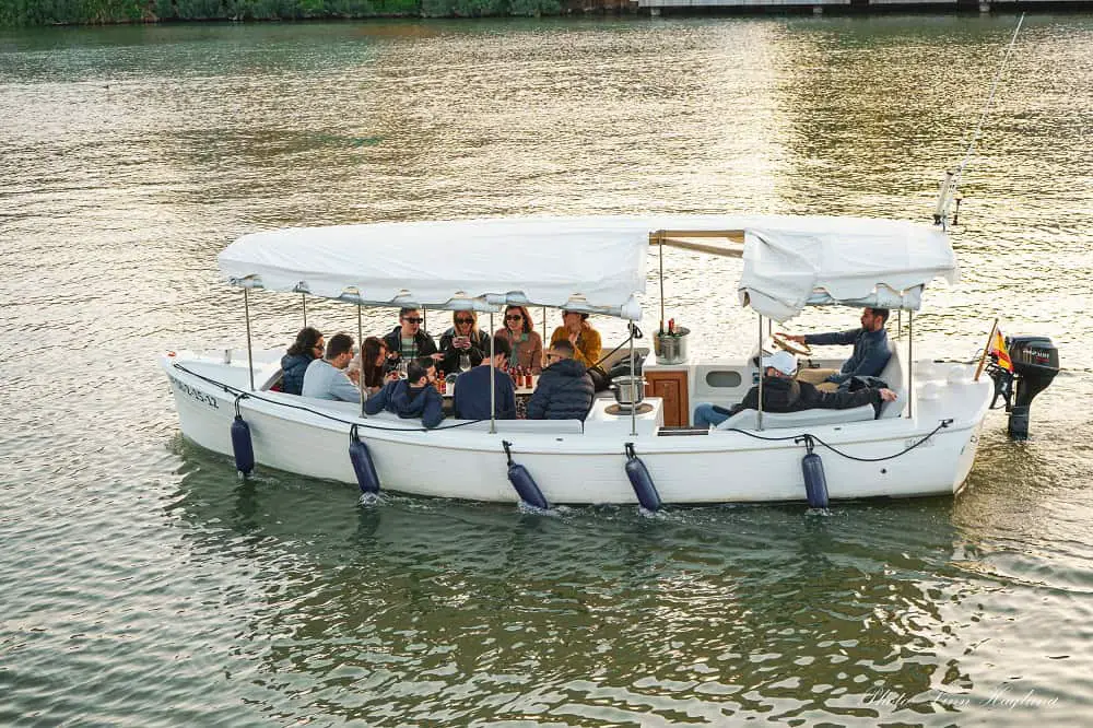 People with jackets, enjoying tapas and drinks on one of the smaller Seville boat crruises on the Guadalquivir River in southern Spain.