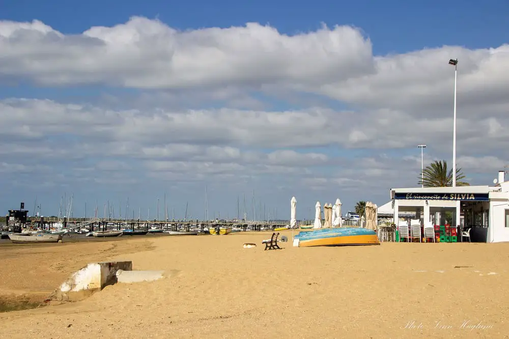 A beach bar at the golden El Rompido Beach where the low tide exposes fishing boats completely. There's also a yellow and turquoise row boat upside down near the chiringuito which brightens the image.