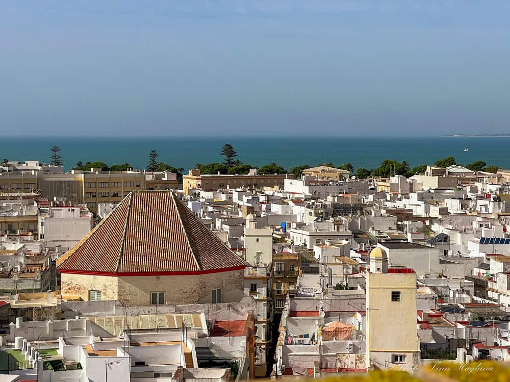 Views from Torre Tavira Cadiz of rooftops leading to the deep blue Atlantic Ocean. A large six-sided tower rooftop dominates the view.