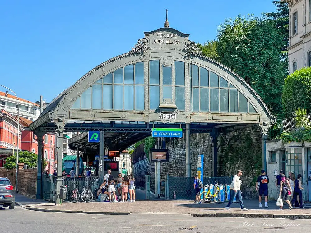 Como historical railway station with people walking in and out on a sunny day. Arriving in Como by train is the most popular way to travel to the beautiul city along Lake Como.