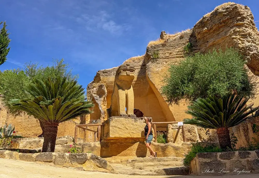 Me, in shorts and singlet, looking up at a giant lion statue that is three times my height in the lush garden of Coto de las Canteras in Osuna, Spain. This is one of many statues and relics on the site that has been recreated from ancient times.